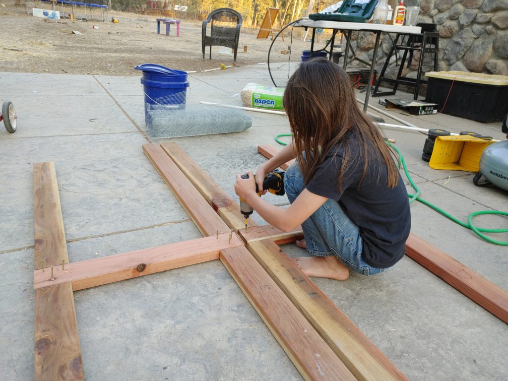 Pre-teen child using a cordless impact driver to put screws into a wooden frame